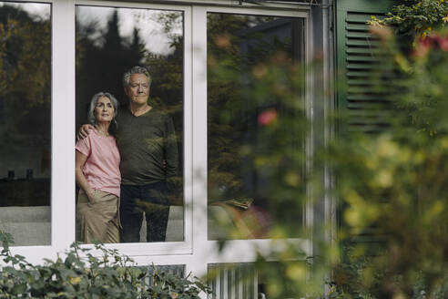 Senior couple behind windowpane of their home looking out - GUSF03063