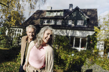 Happy senior couple in garden of their home in autumn - GUSF03066