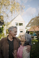 Happy senior couple in garden of their home in autumn - GUSF03068