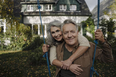 Porträt einer glücklichen Frau, die einen älteren Mann auf einer Schaukel im Garten umarmt - GUSF03071