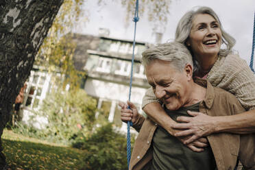 Glückliche Frau umarmt älteren Mann auf einer Schaukel im Garten - GUSF03072