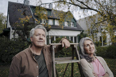 Senior couple with a ladder in garden of their home - GUSF03078