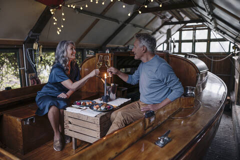 Senior couple having a candlelight dinner on a boat in boathouse clinking champagne glasses stock photo