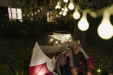 Senior couple camping in garden of their home at night - GUSF03096