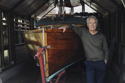 Porträt eines stolzen älteren Mannes an einem Holzboot in einem Bootshaus - GUSF03101