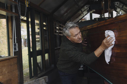 Senior man cleaning wooden boat in a boathouse - GUSF03103