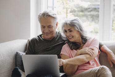 Happy senior couple with laptop relaxing on couch at home - GUSF03110