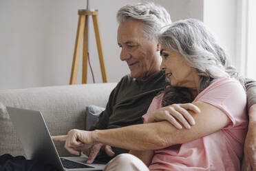 Senior couple with laptop relaxing on couch at home - GUSF03111