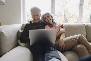 Glückliches älteres Paar mit Laptop, das sich zu Hause auf der Couch entspannt - GUSF03112