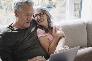 Happy senior couple with laptop relaxing on couch at home - GUSF03113