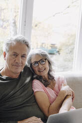 Portrait of senior couple with laptop relaxing on couch at home - GUSF03114