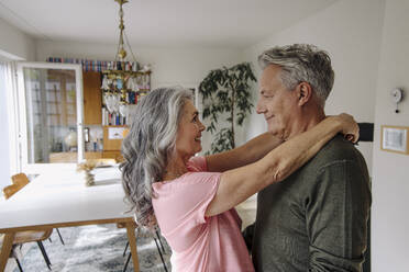 Happy senior couple embracing in living room at home - GUSF03117