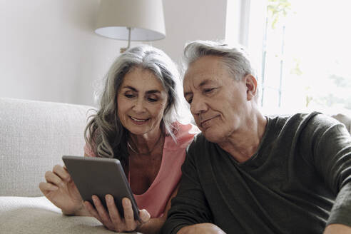 Glückliches älteres Paar, das sich zu Hause auf der Couch entspannt und ein Tablet benutzt - GUSF03122