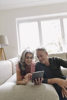 Glückliches älteres Paar, das sich zu Hause auf der Couch entspannt und ein Tablet benutzt - GUSF03123
