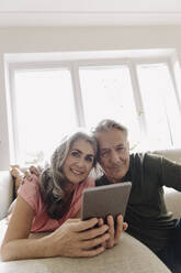 Porträt eines glücklichen älteren Paares, das sich zu Hause auf der Couch mit einem Tablet entspannt - GUSF03124