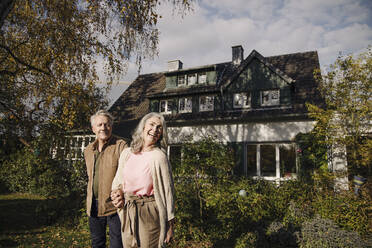 Happy senior couple in garden of their home in autumn - GUSF03131