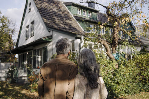 Rear view of senior couple in garden of their home in autumn - GUSF03137