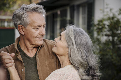 Affectionate senior couple in garden of their home in autumn - GUSF03139