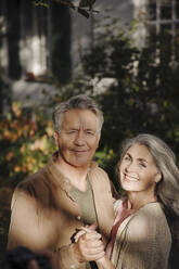 Porträt eines glücklichen älteren Paares im Garten ihres Hauses im Herbst - GUSF03140