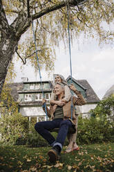 Happy woman embracing senior man on a swing in garden - GUSF03141