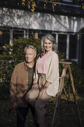 Senior couple with a ladder in garden of their home - GUSF03146