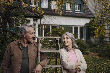 Senior couple with a ladder in garden of their home - GUSF03148