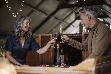 Senior couple having a candlelight dinner on a boat in boathouse clinking champagne glasses - GUSF03150