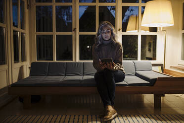 Reife Frau benutzt Tablet auf Couch zu Hause in der Dunkelheit - GUSF03160