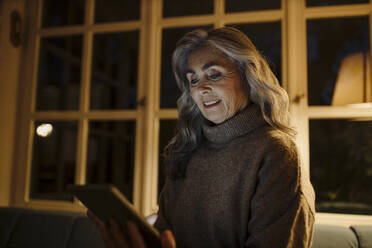 Reife Frau benutzt Tablet auf Couch zu Hause in der Dunkelheit - GUSF03162
