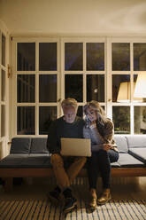 Senior couple using laptop on couch at home at night - GUSF03167