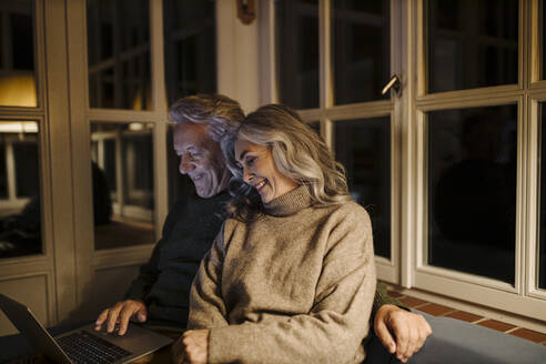 Senior couple using laptop on couch at home at night - GUSF03169