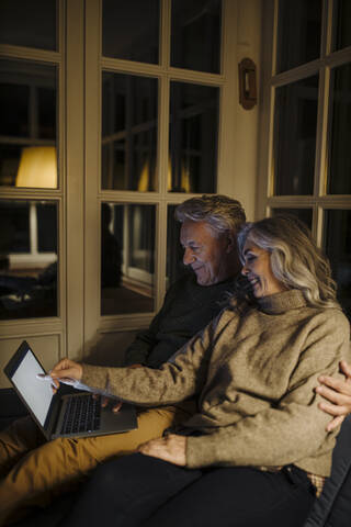 Älteres Ehepaar benutzt nachts einen Laptop auf der Couch zu Hause, lizenzfreies Stockfoto