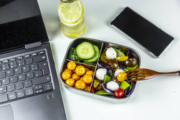 Laptop, smart phone, bottle of lemonade and lunchbox with cucumber slices, winter cherries and quinoa salad (quinoa, cherry tomato, red cabbage, sugar snap peas and mozzarella balls) - SARF04410