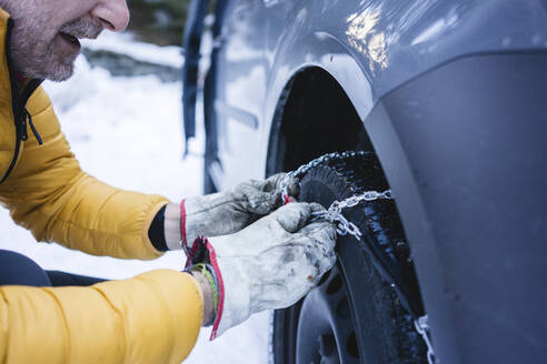 Man putting the snow chains on his car - MRAF00461