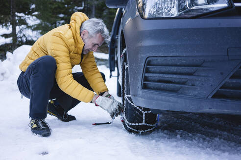 Man putting the snow chains on his car - MRAF00462