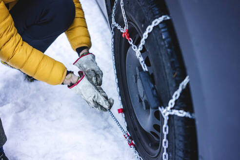 Man putting the snow chains on his car - MRAF00463