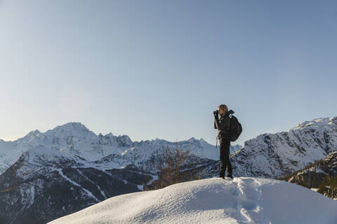 Frau beim Fotografieren einer winterlichen Berglandschaft, Valmalenco, Italien, lizenzfreies Stockfoto