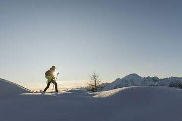 Frau geht mit Schneeschuhen im frischen Schnee in den Bergen bei Sonnenuntergang, Valmalenco, Italien - MRAF00483