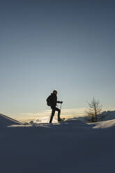 Frau geht mit Schneeschuhen im frischen Schnee in den Bergen bei Sonnenuntergang, Valmalenco, Italien - MRAF00484