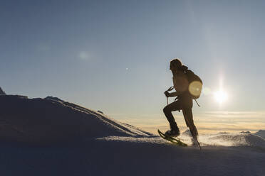 Frau geht mit Schneeschuhen im frischen Schnee in den Bergen bei Sonnenuntergang, Valmalenco, Italien - MRAF00485