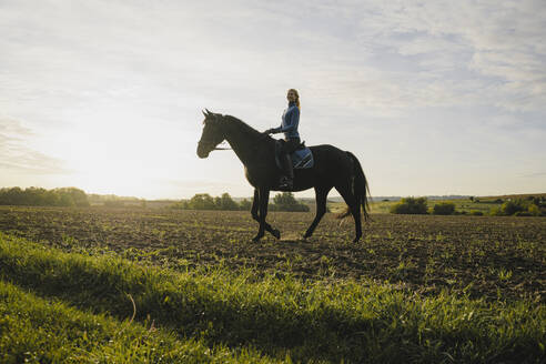Frau reitet Pferd auf einem Feld auf dem Lande bei Sonnenuntergang - JOSF04121