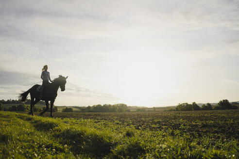 Frau reitet Pferd auf einem Feld auf dem Lande bei Sonnenuntergang - JOSF04130