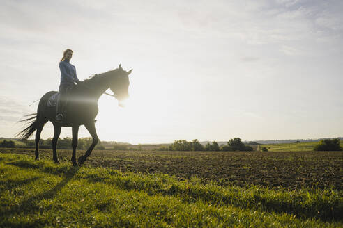 Frau reitet Pferd auf einem Feld auf dem Lande bei Sonnenuntergang - JOSF04131