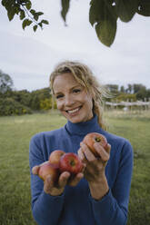 Pirtrait of smiling young woman holding apples in the countryside - JOSF04140