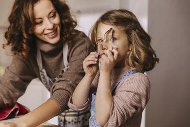 Playful girl with her mother holding Christmas cookie cutter in kitchen - MFF04943