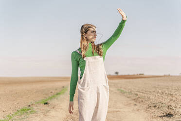 Young woman standing on dry field, shielding eyes - ERRF02296