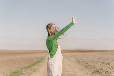 Young woman standing on dry field, shielding eyes - ERRF02297