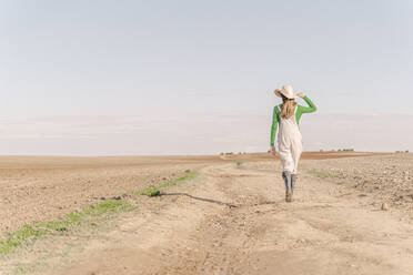 Junge Frau geht auf trockenem Feld, Rückansicht - ERRF02301