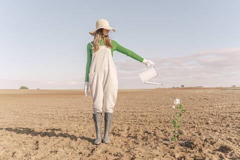 Woamn steht auf kargem Feld und gießt Blumen, lizenzfreies Stockfoto