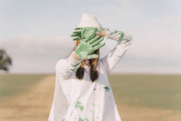 Junge Frau hält sich die grün bemalten Hände vor das Gesicht - ERRF02377